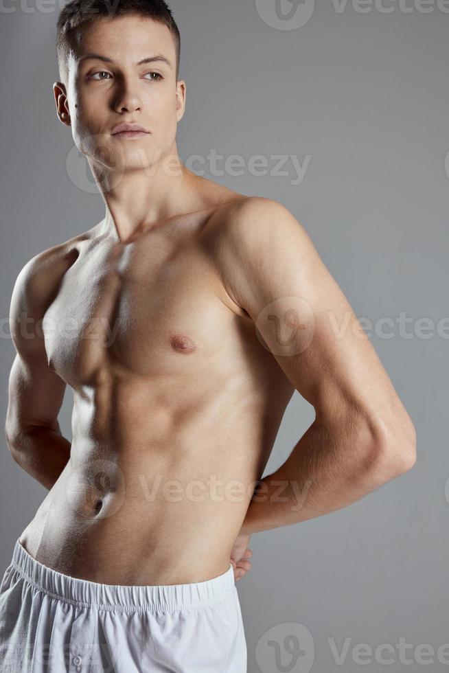 athlete with pumped up abs holding hands behind his back on gray background cropped view photo