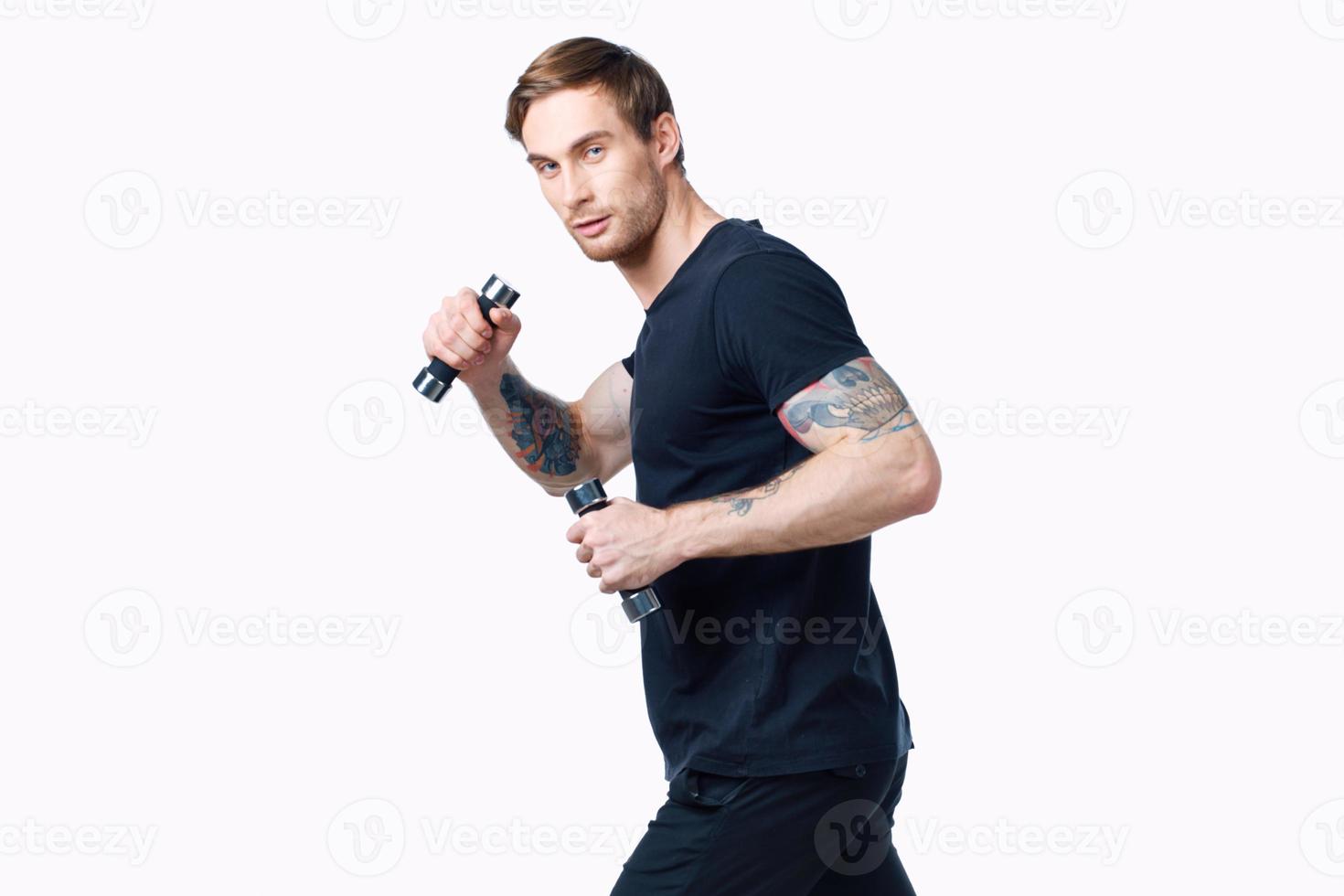 nice guy with dumbbells in a black t-shirt and trousers goes in for sports side view photo