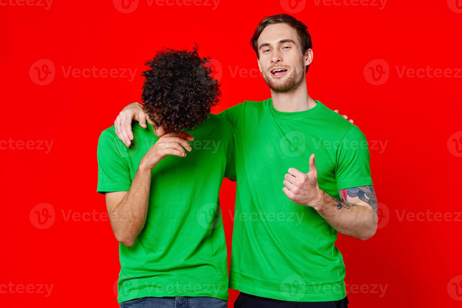 two friends in green t-shirts hugs fun red background photo