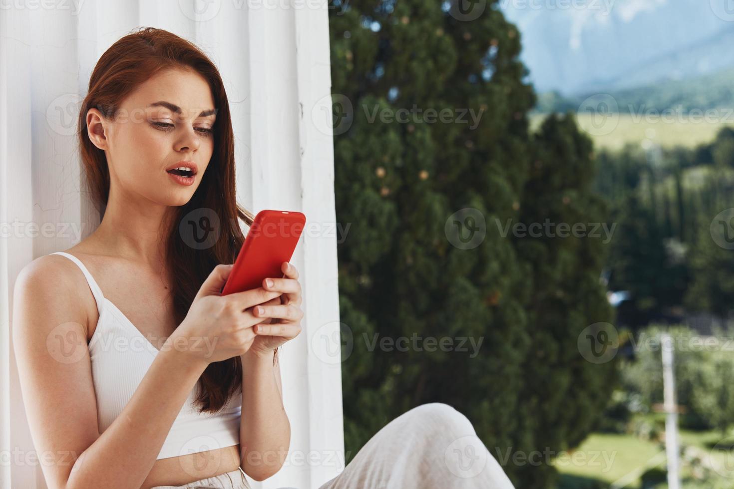hermosa mujer utilizar el teléfono mira a el pantalla en un cómodo hotel un abierto ver de el montaña ver foto