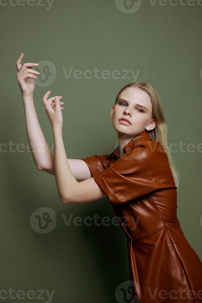 Professional blonde young female model in brown trendy dress holding hands up serious looks at camera curving dancing posing isolated on over olive green studio wall background. Seasonal sale banner photo