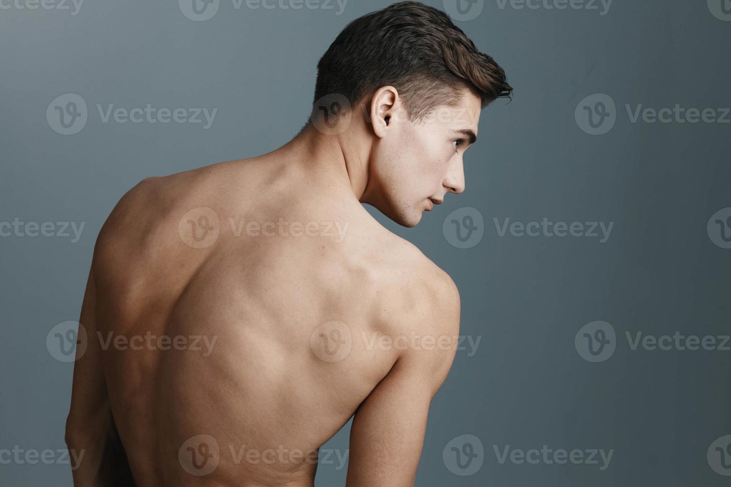 sexy hombre con un desnudo espalda mira a el lado en un gris antecedentes posterior ver de un aptitud deporte modelo foto