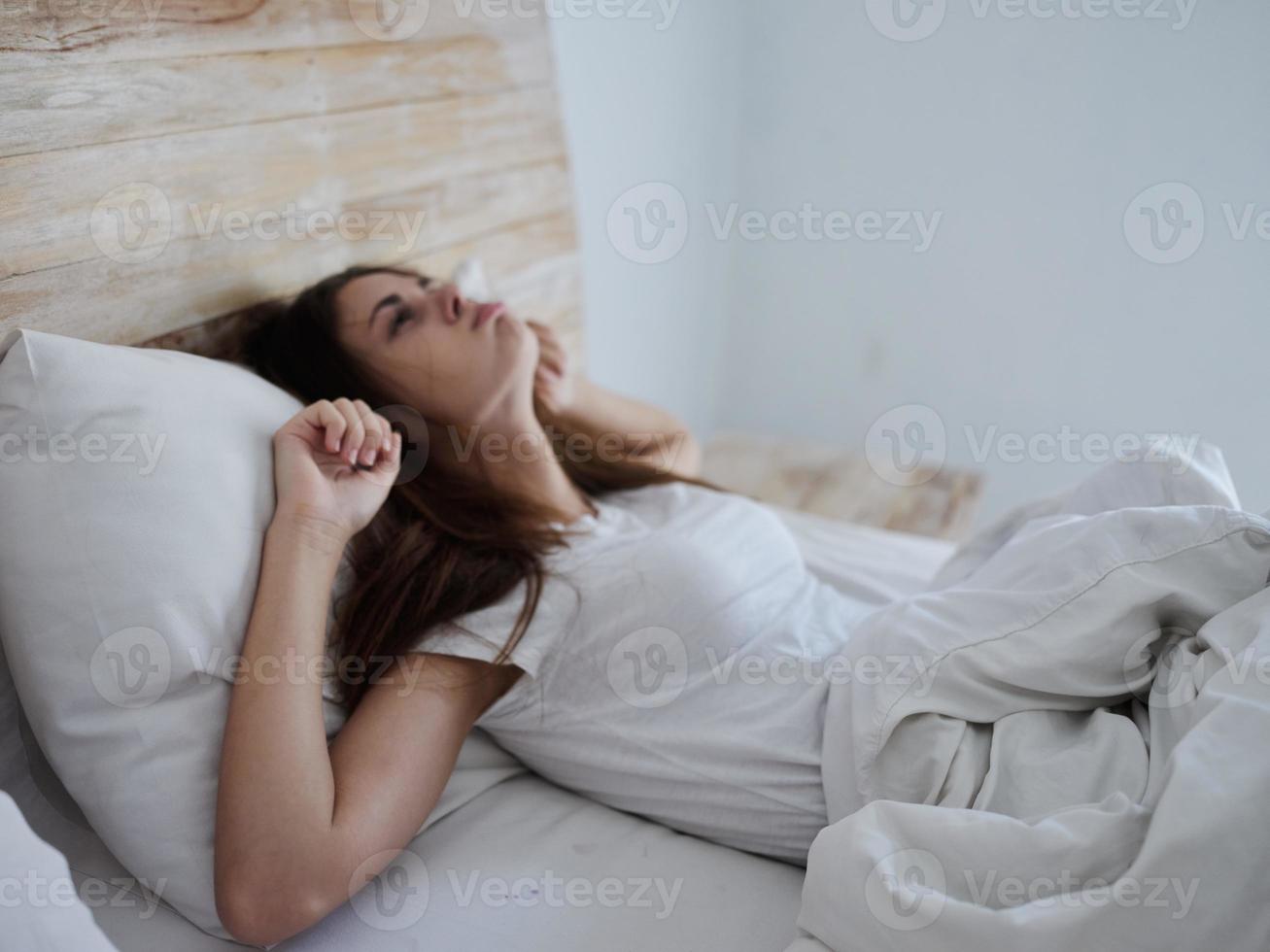 woman looking at the ceiling lying in bed covered with a blanket health problems photo