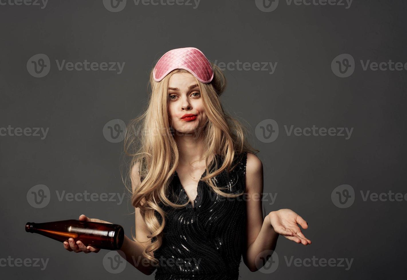 Drunk woman with a bottle in her hand black dress pink sleep mask photo