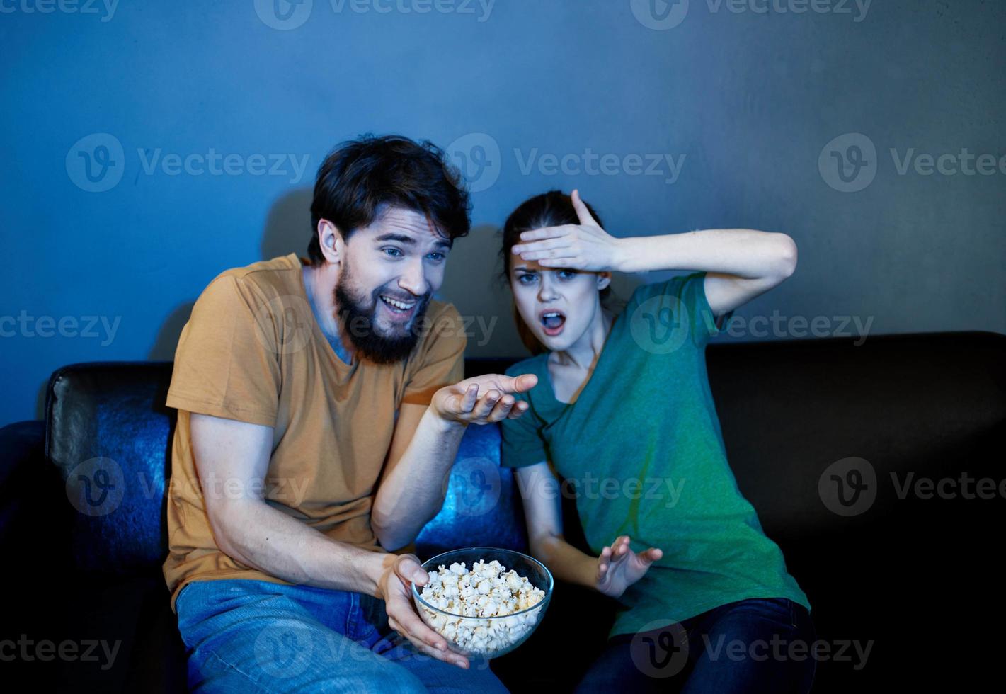 un hombre y un asustado mujer acecho un película en el noche en el sofá con un plato de palomitas de maíz foto