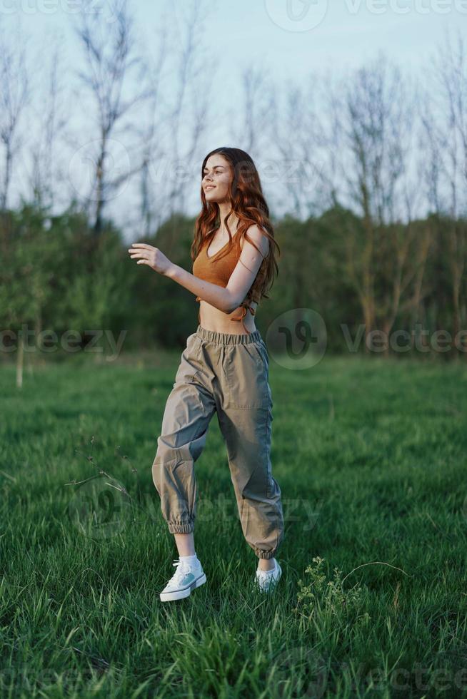 A young woman in a top and green pants and athletic sneakers is jogging on the summer green grass with her hair loose photo