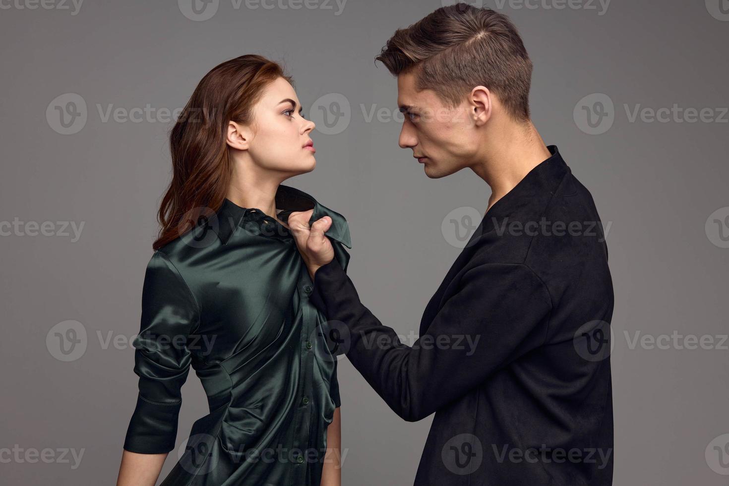 A frightened woman in a dress is looking at an aggressive man on a gray background photo