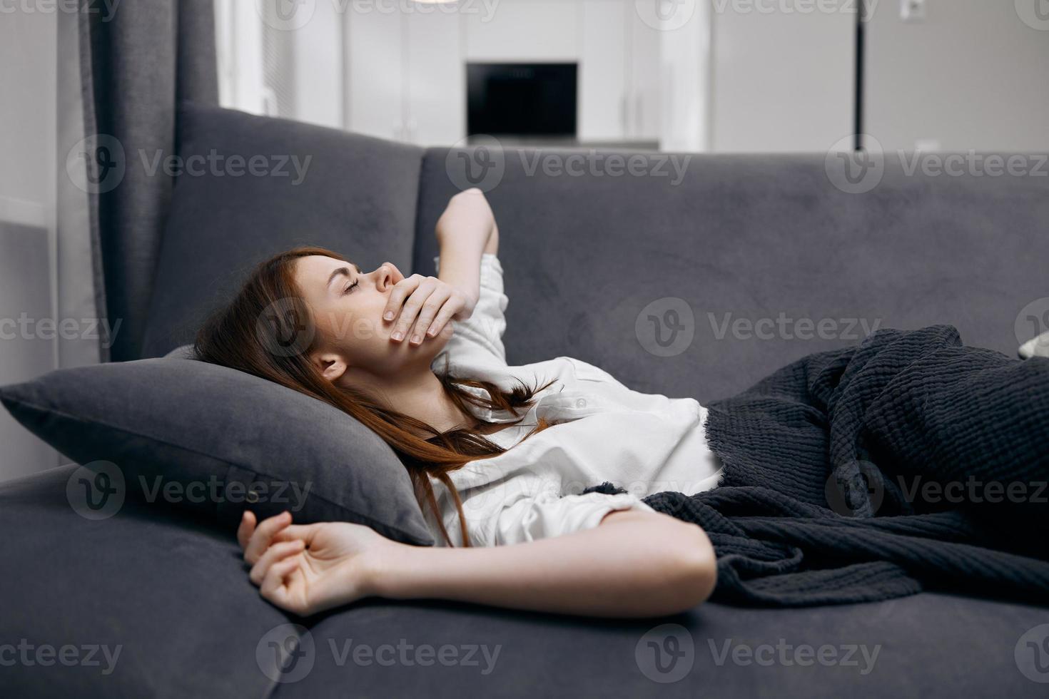 woman covers her face with her hand while lying on the couch at home health problems photo