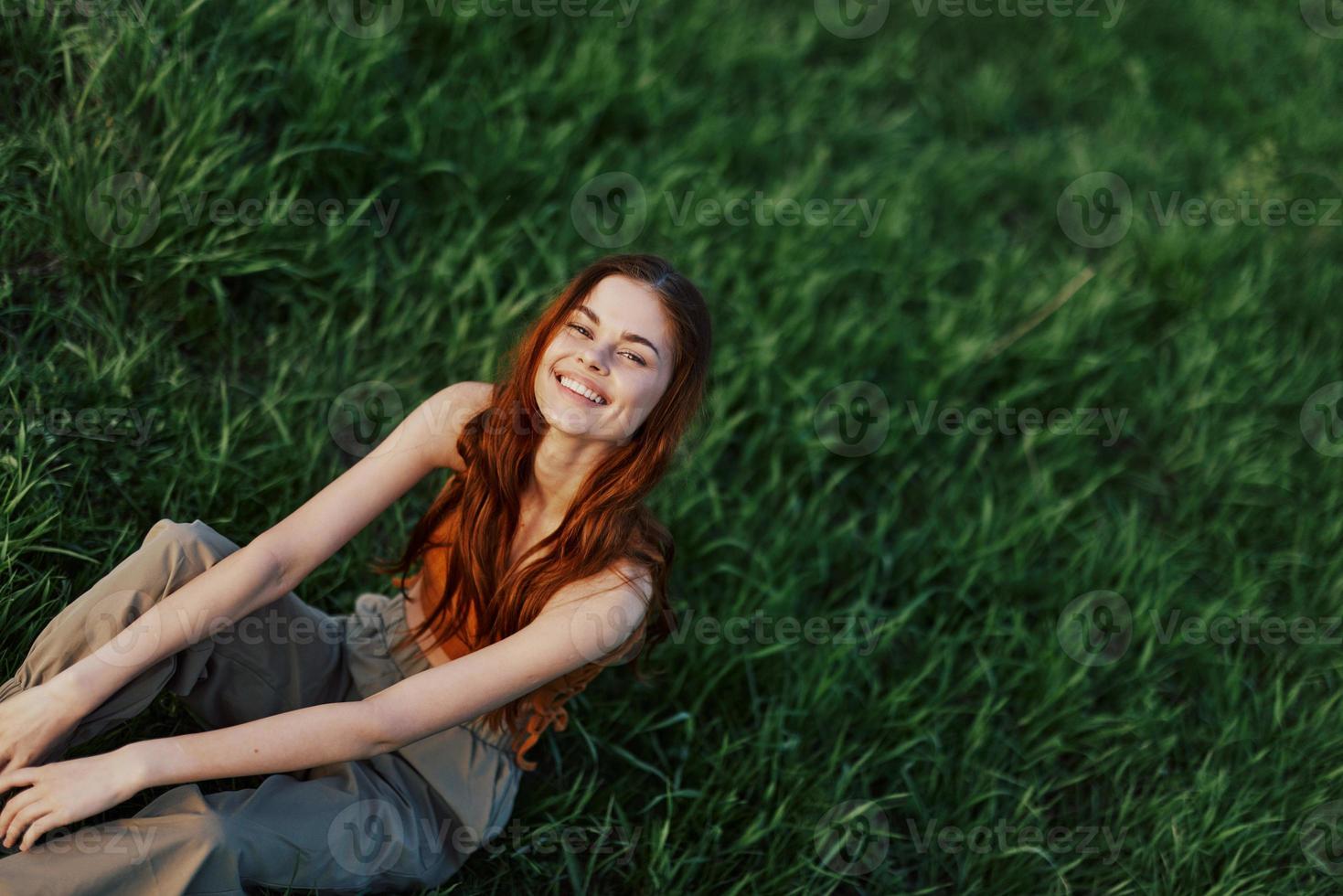 Happy woman smiling beautifully and looking up at the camera sitting on fresh green grass in the summer sunshine photo