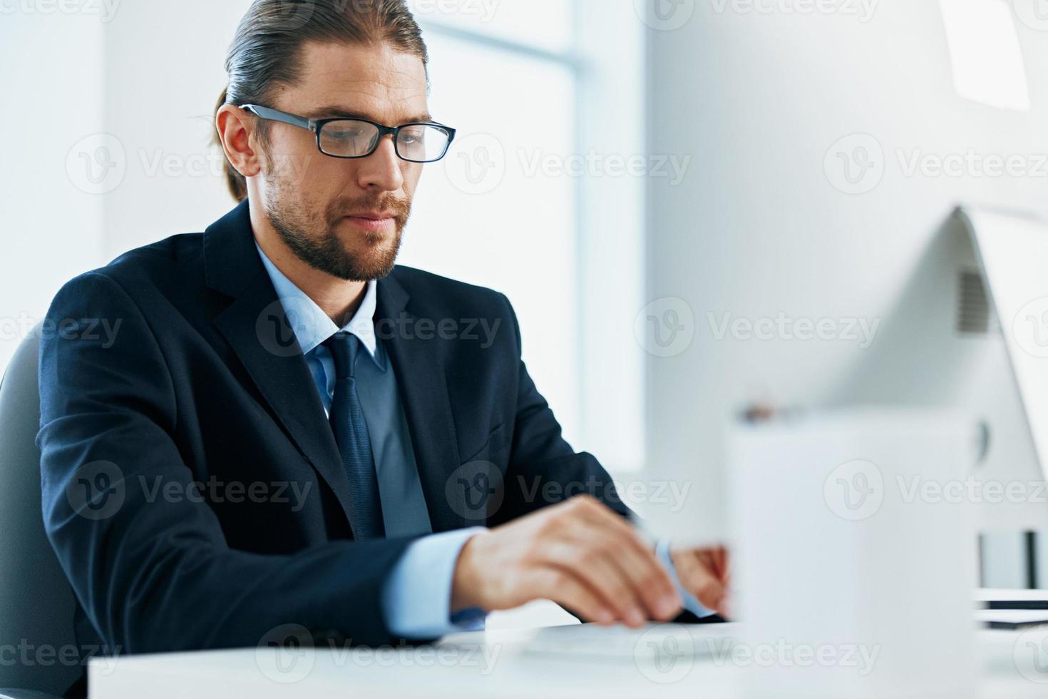 a man in a suit with glasses typing at his desk photo