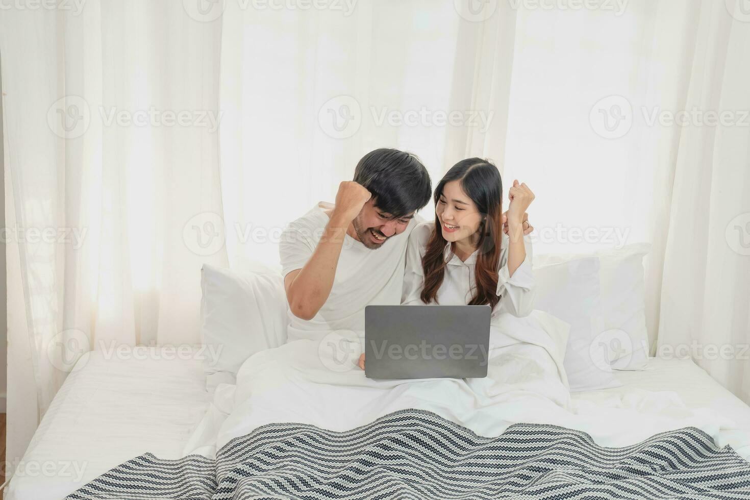 Young happy asian couple using laptop in bed watching movie, romantic time to enhance family relationship, family concept. photo