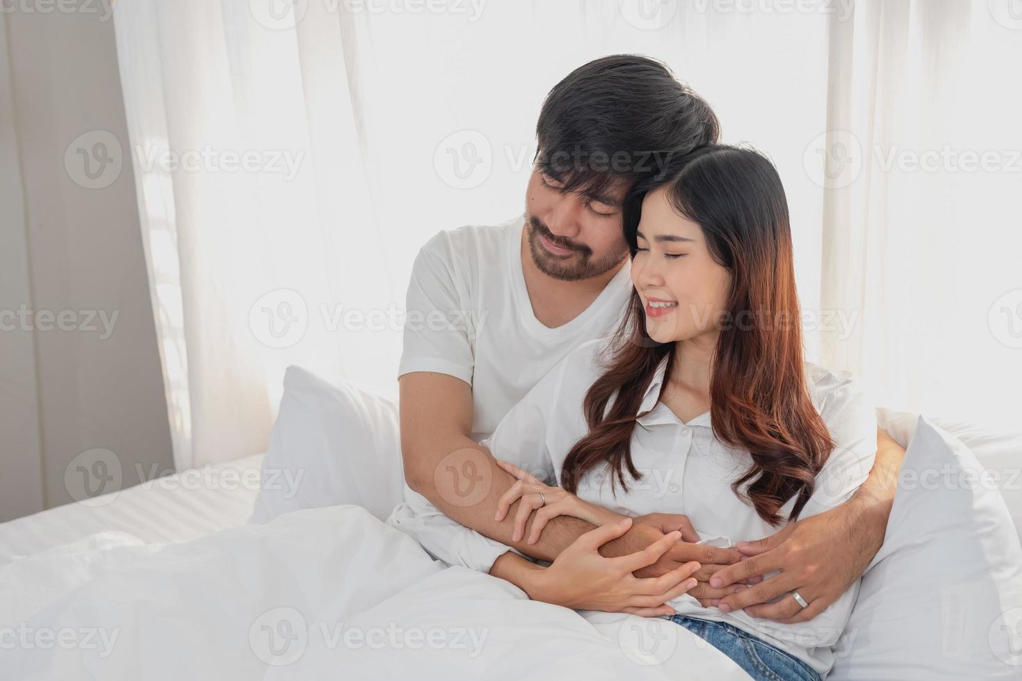 Happy young asian couple embracing, teasing, playing cheerfully in bed at home, romantic time to enhance family bonding. family concept. photo