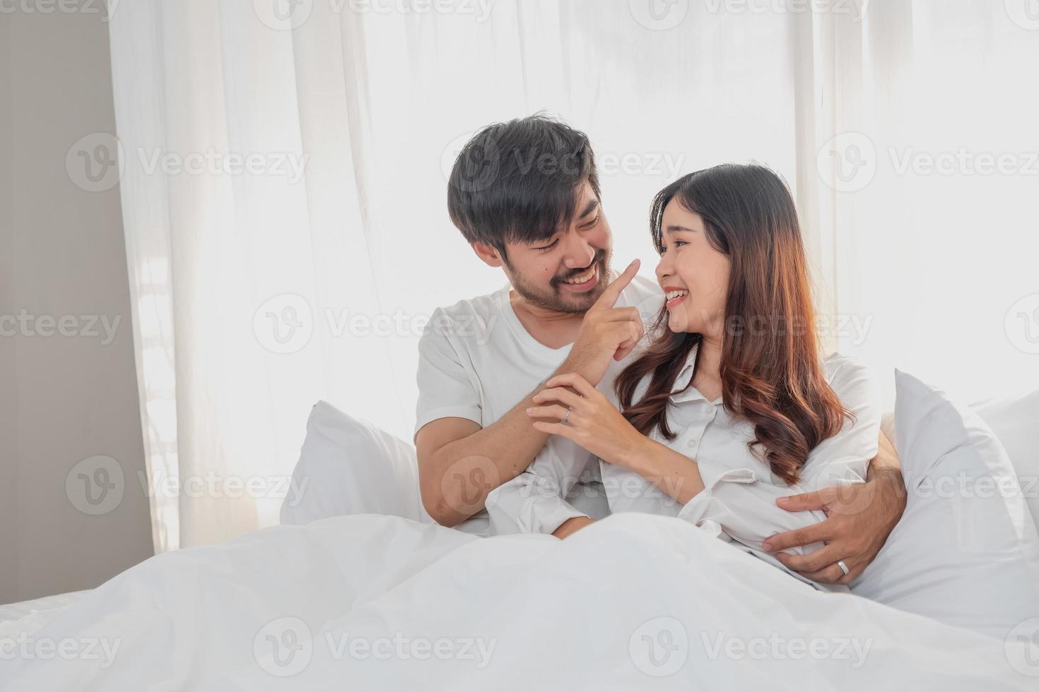 contento joven asiático Pareja abrazando, broma, jugando alegremente en cama a hogar, romántico hora a mejorar familia vinculación familia concepto. foto