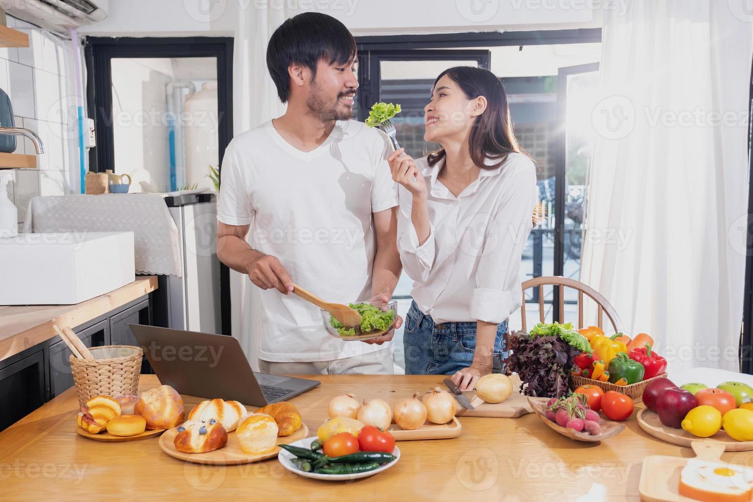 joven asiático Pareja Cocinando con frutas y vegetales y utilizando ordenador portátil en el cocina a cocinar comida juntos dentro el familia felizmente, familia concepto. foto