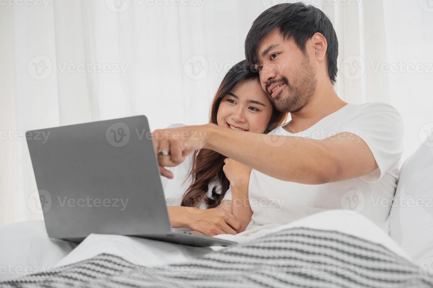 Young happy asian couple using laptop in bed watching movie, romantic time to enhance family relationship, family concept. photo