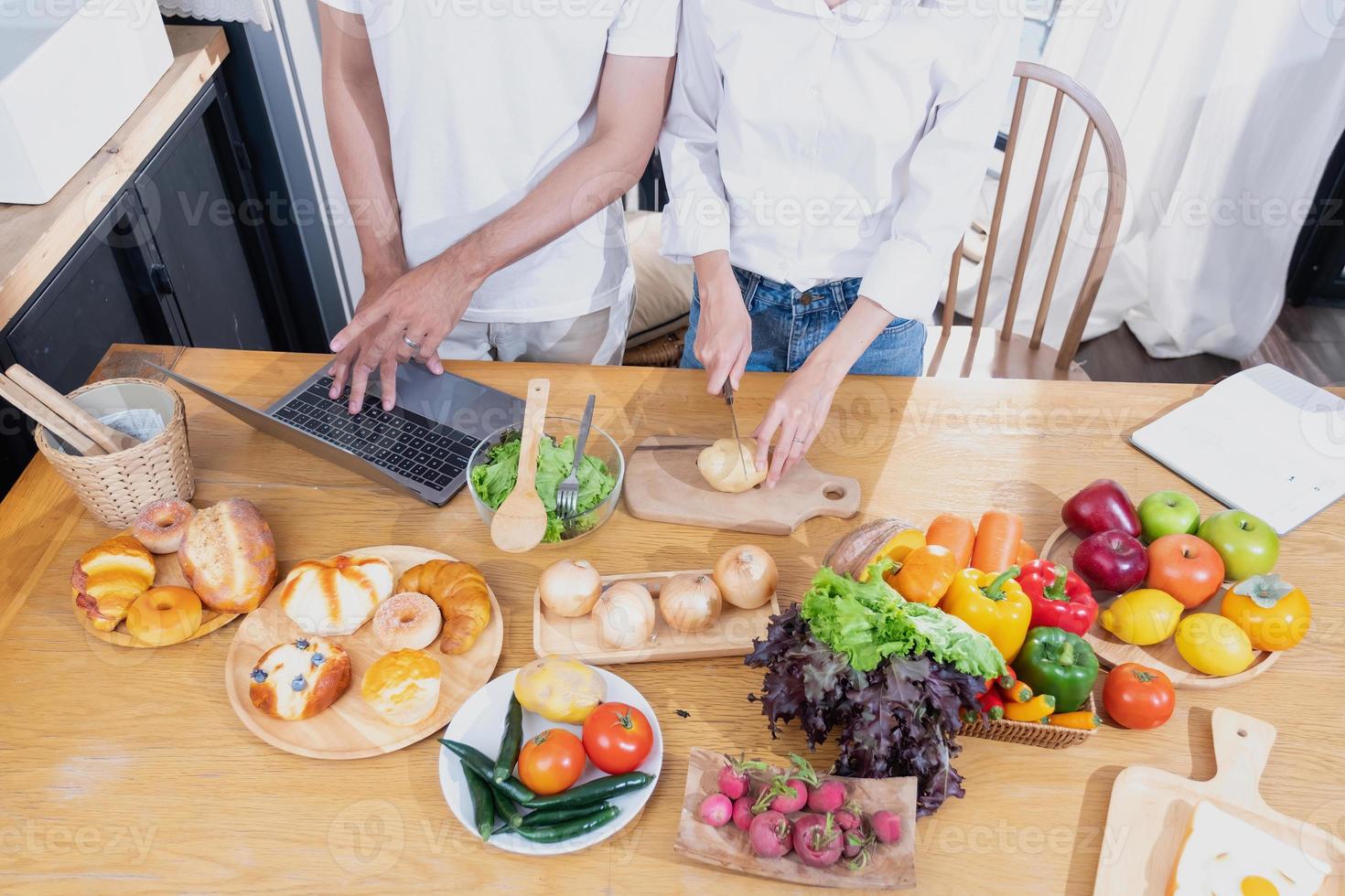 joven asiático Pareja Cocinando con frutas y vegetales y utilizando ordenador portátil en el cocina a cocinar comida juntos dentro el familia felizmente, familia concepto. foto