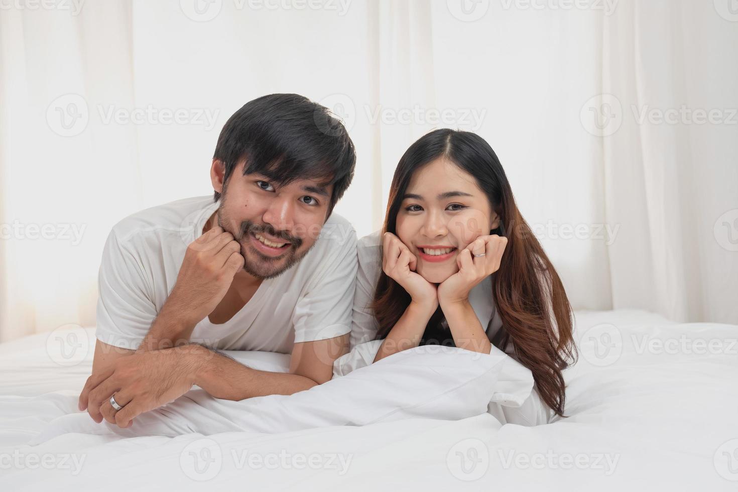 Happy young asian couple embracing, teasing, playing cheerfully in bed at home, romantic time to enhance family bonding. family concept. photo