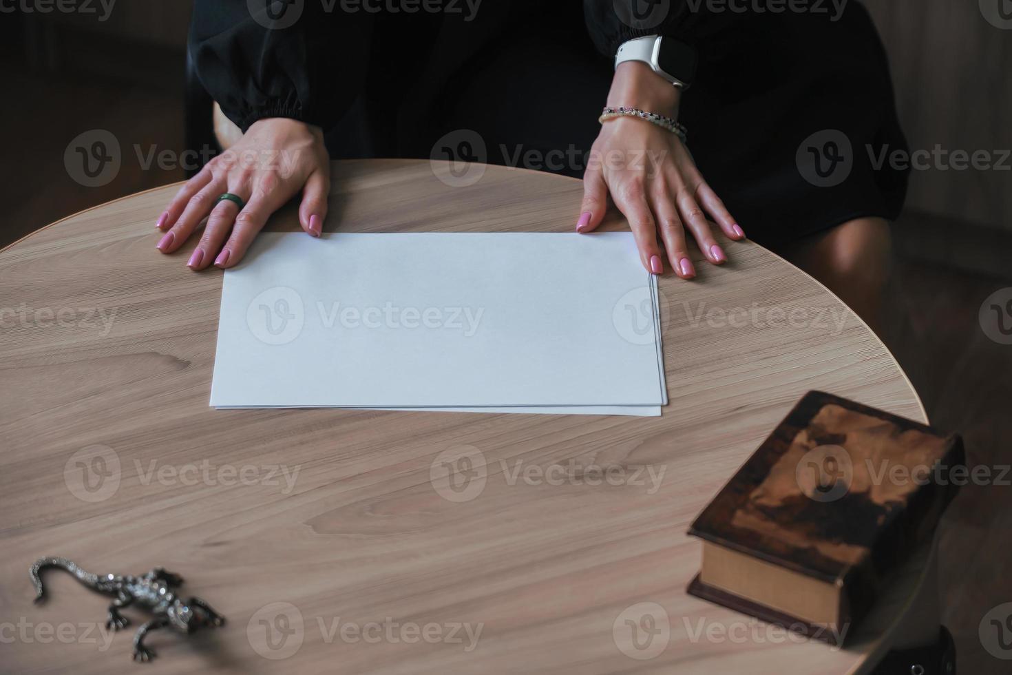 The hands of a young woman hold a blank sheet of paper on a wooden table. Mockup, copy space photo