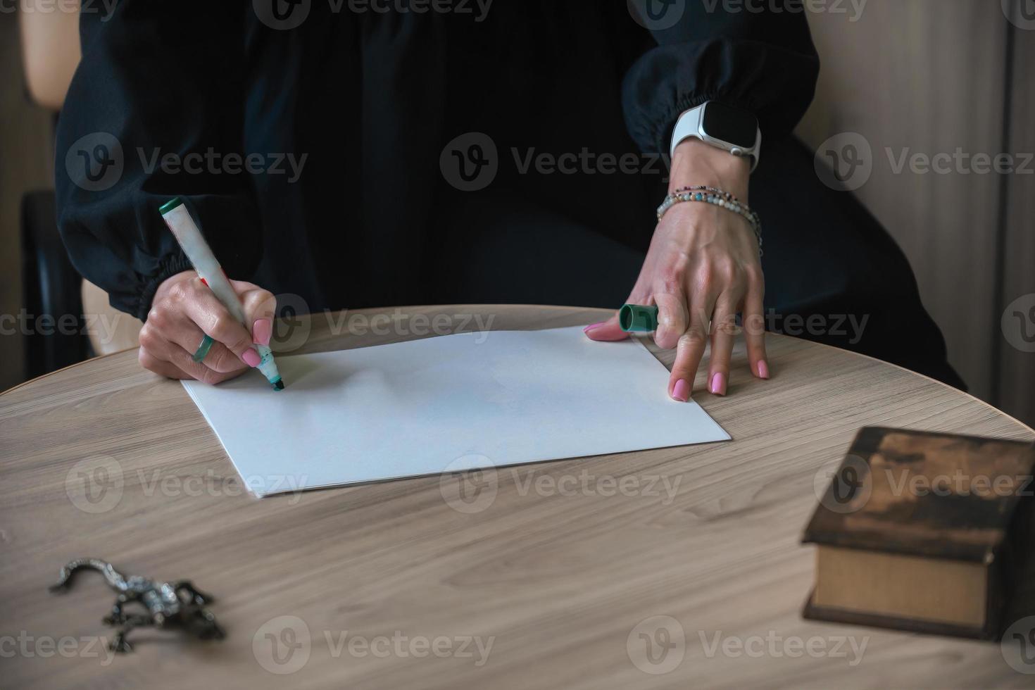 The hands of a young woman write on a blank sheet of paper on a wooden table. Mockup, copy space photo