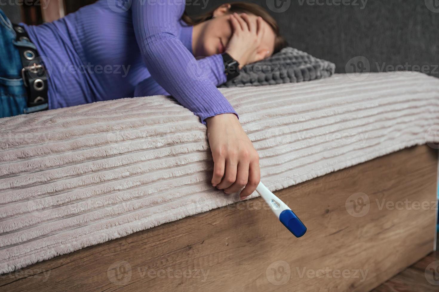 a young woman lies on the bed, she covered her face with her hand and cries, in her other hand there is a negative pregnancy test. A woman's desire to have children, copy space photo