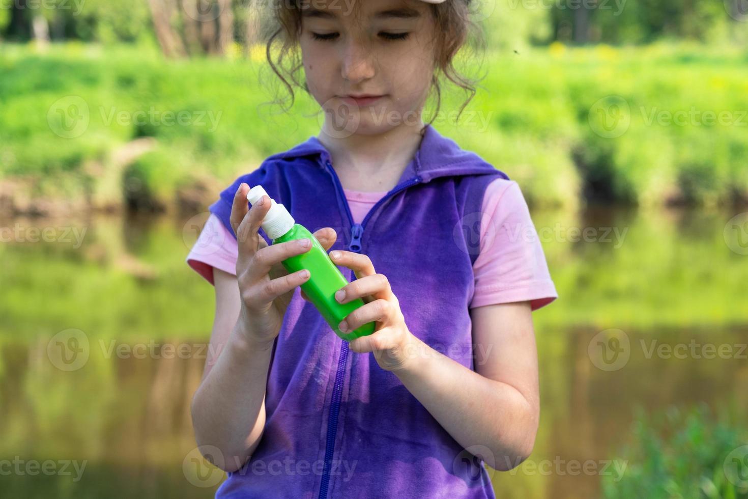 Girl sprays mosquito spray on the skin in nature that bite her hands and feet. Protection from insect bites, repellent safe for children. Outdoor recreation, against allergies. Summer time photo