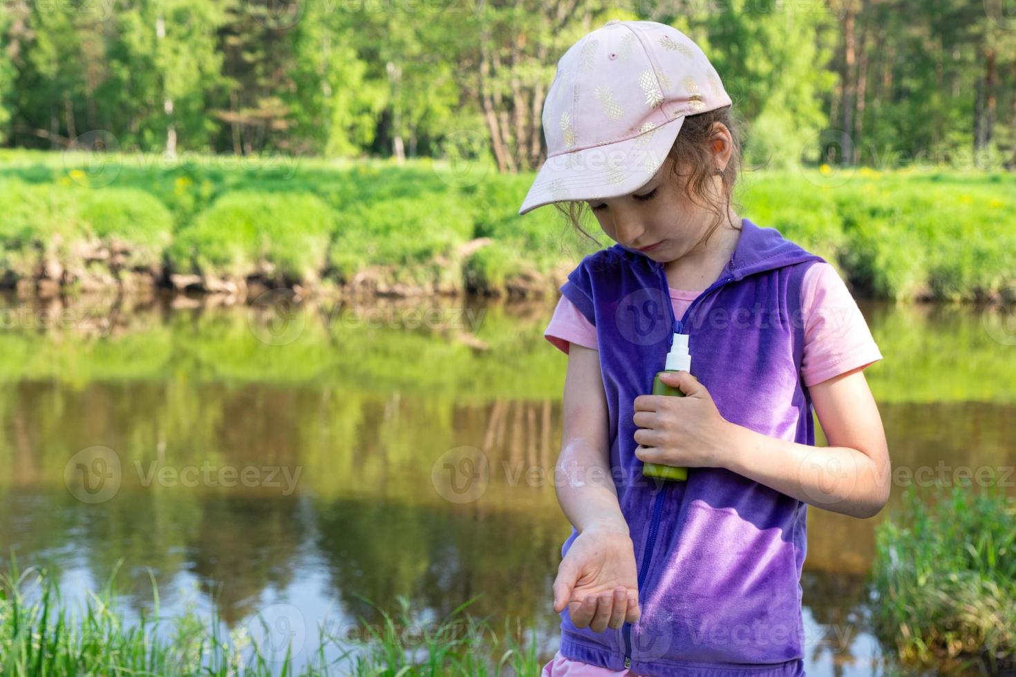 Girl sprays mosquito spray on the skin in nature that bite her hands and feet. Protection from insect bites, repellent safe for children. Outdoor recreation, against allergies. Summer time photo
