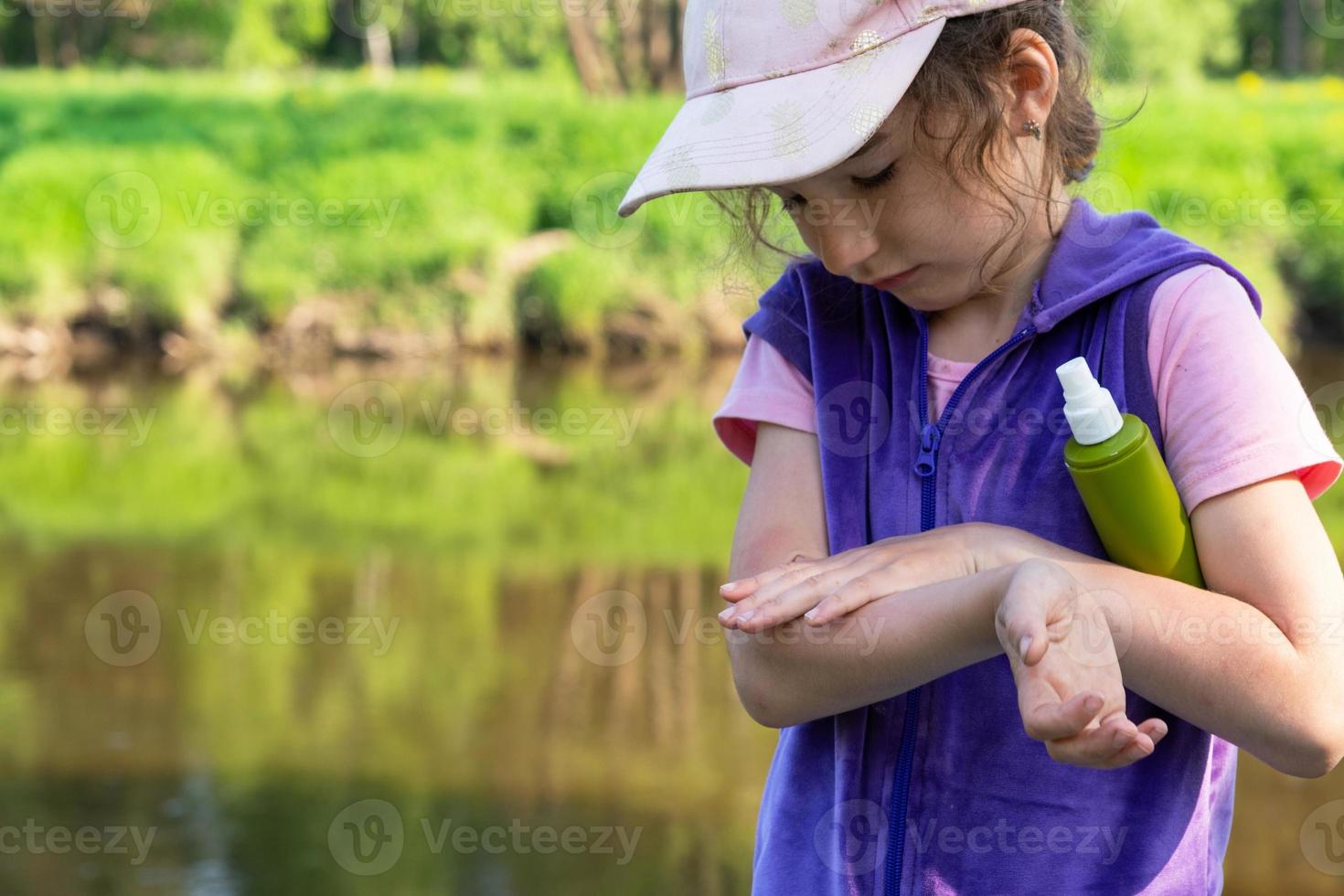 Girl sprays mosquito spray on the skin in nature that bite her hands and feet. Protection from insect bites, repellent safe for children. Outdoor recreation, against allergies. Summer time photo