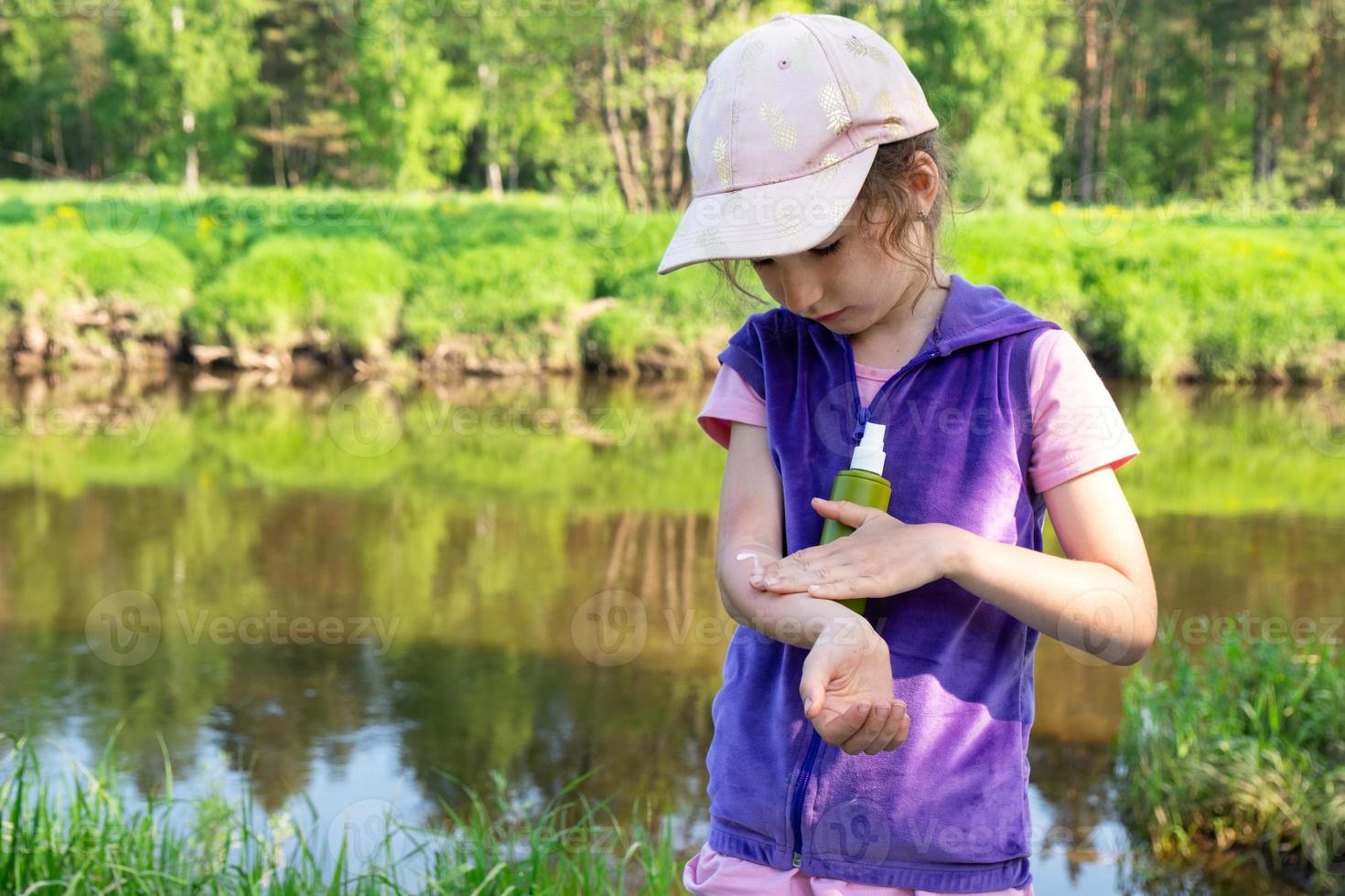 Girl sprays mosquito spray on the skin in nature that bite her hands and feet. Protection from insect bites, repellent safe for children. Outdoor recreation, against allergies. Summer time photo