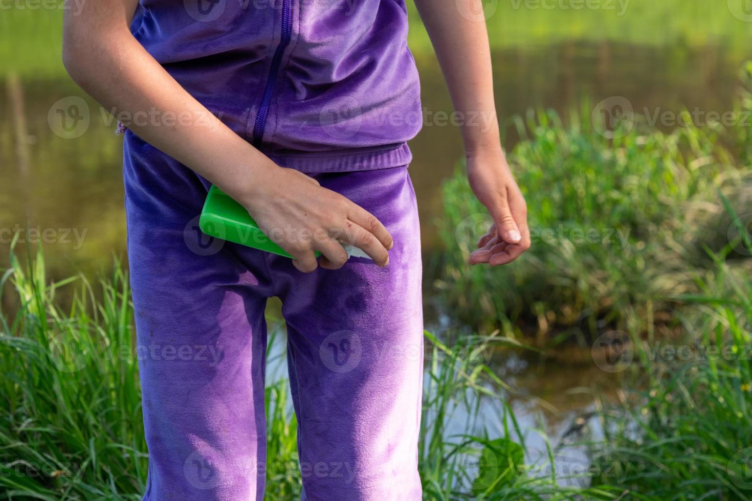 Girl sprays mosquito spray on the skin in nature that bite her hands and feet. Protection from insect bites, repellent safe for children. Outdoor recreation, against allergies. Summer time photo