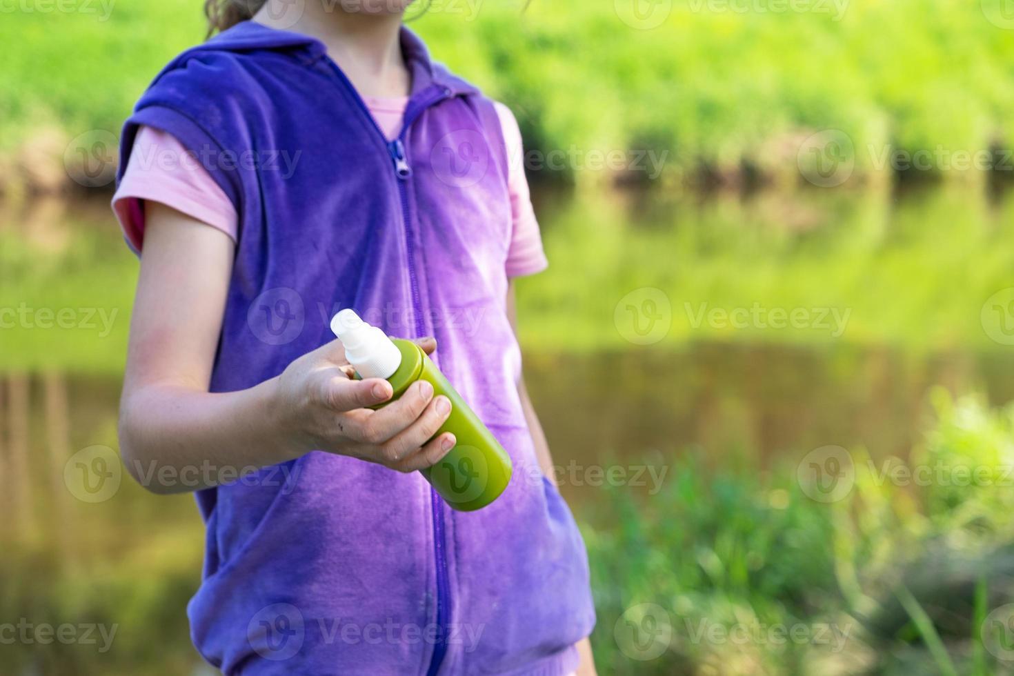 Girl sprays mosquito spray on the skin in nature that bite her hands and feet. Protection from insect bites, repellent safe for children. Outdoor recreation, against allergies. Summer time photo