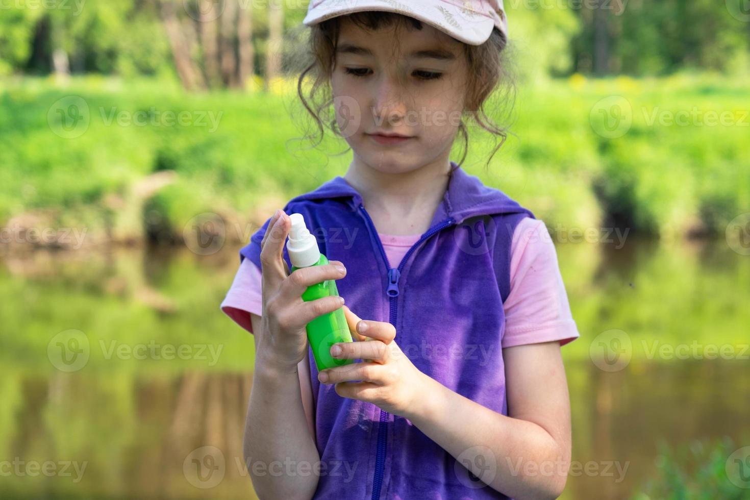 Girl sprays mosquito spray on the skin in nature that bite her hands and feet. Protection from insect bites, repellent safe for children. Outdoor recreation, against allergies. Summer time photo