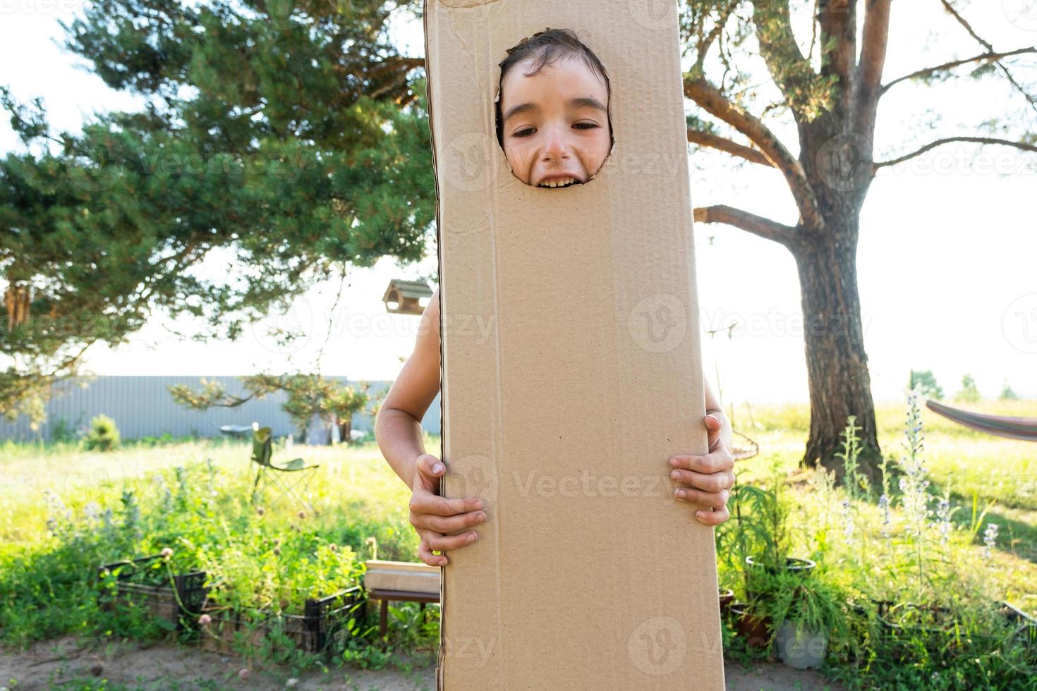 el niño es gracioso bailando y engañando alrededor en un caja disfraz - redondo separar para cara y manos. Moviente a un nuevo casa, para niños juegos desde improvisado medio, un traje con tu propio manos foto