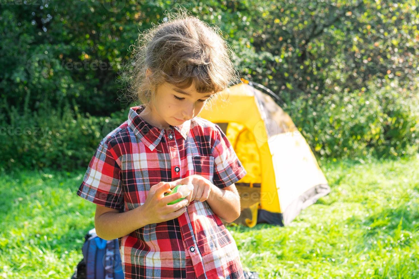 Girl sprays mosquito spray on the skin in nature that bite her hands and feet. Protection from insect bites, repellent safe for children. Outdoor recreation, against allergies. Summer time photo