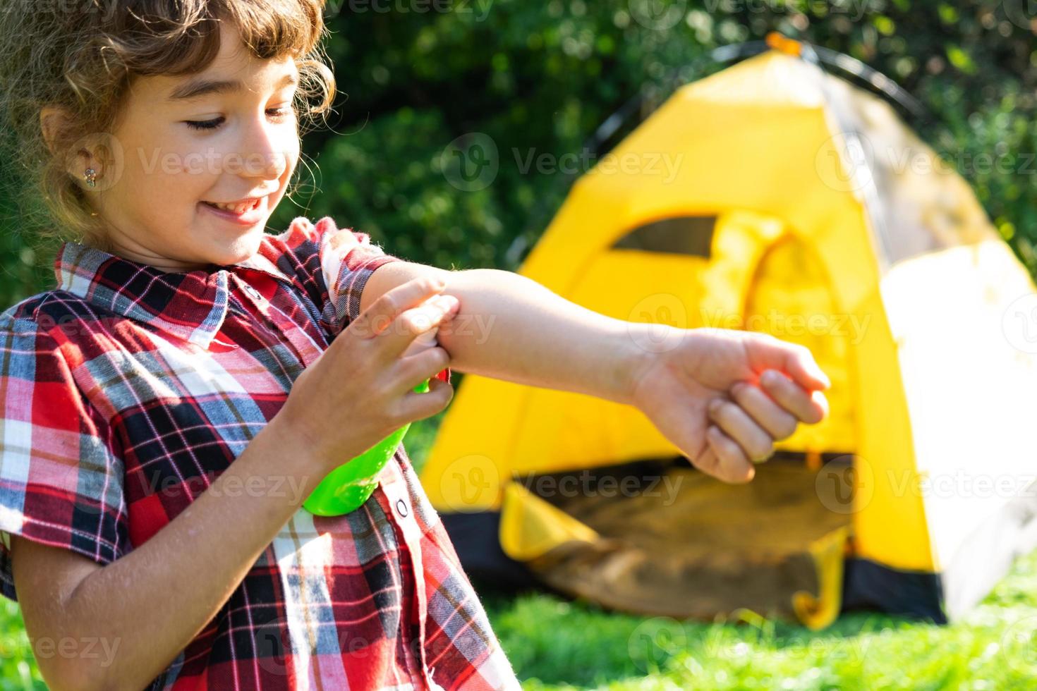 Girl sprays mosquito spray on the skin in nature that bite her hands and feet. Protection from insect bites, repellent safe for children. Outdoor recreation, against allergies. Summer time photo