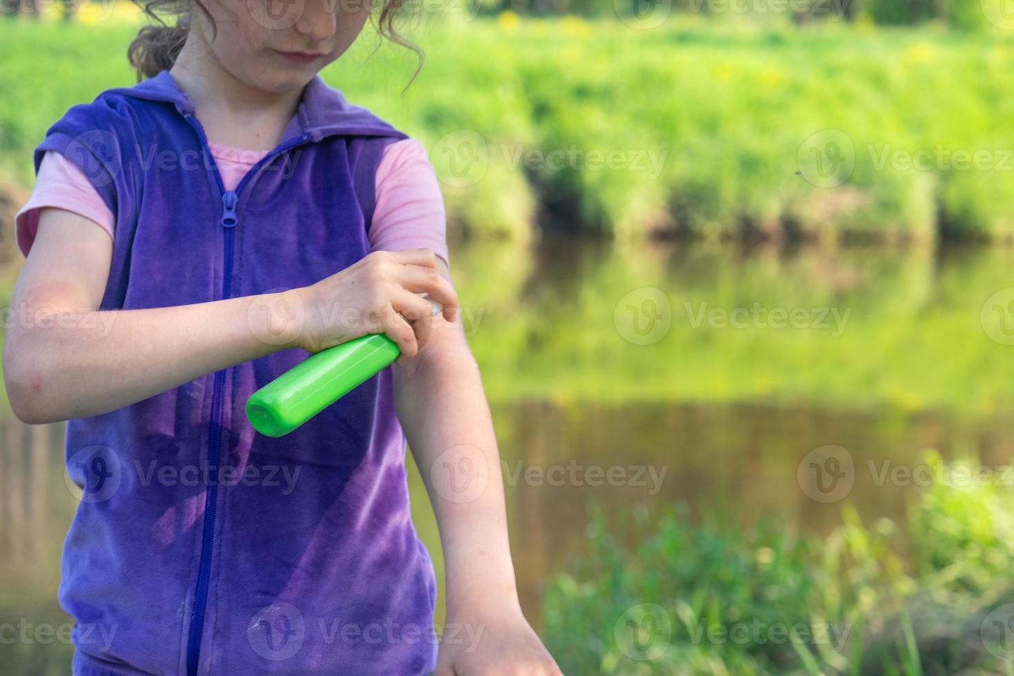 Girl sprays mosquito spray on the skin in nature that bite her hands and feet. Protection from insect bites, repellent safe for children. Outdoor recreation, against allergies. Summer time photo