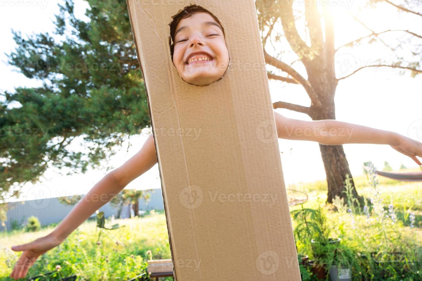 el niño es gracioso bailando y engañando alrededor en un caja disfraz - redondo separar para cara y manos. Moviente a un nuevo casa, para niños juegos desde improvisado medio, un traje con tu propio manos foto