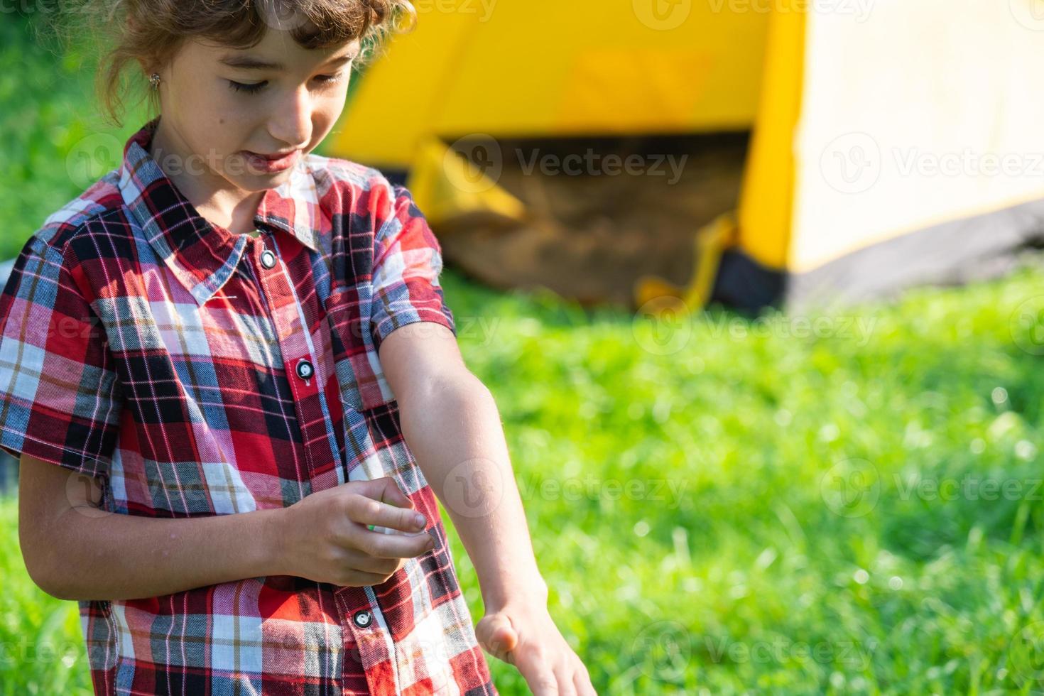 Girl sprays mosquito spray on the skin in nature that bite her hands and feet. Protection from insect bites, repellent safe for children. Outdoor recreation, against allergies. Summer time photo