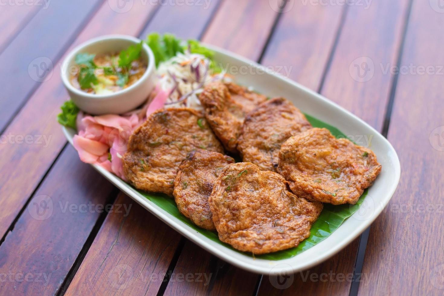 Top view. Fried fish paste balls or deep fried fish cake Contains curry paste as ingredient It is spicy Thai dish served with dipping sauce mixed with cucumber. Asian food style. photo