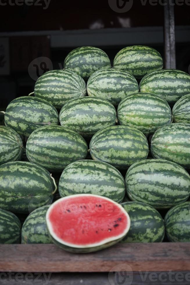The neatly arranged pile of watermelons with one fruit cut open revealing its red flesh. These watermelons are being sold at a fruit market in Thailand photo