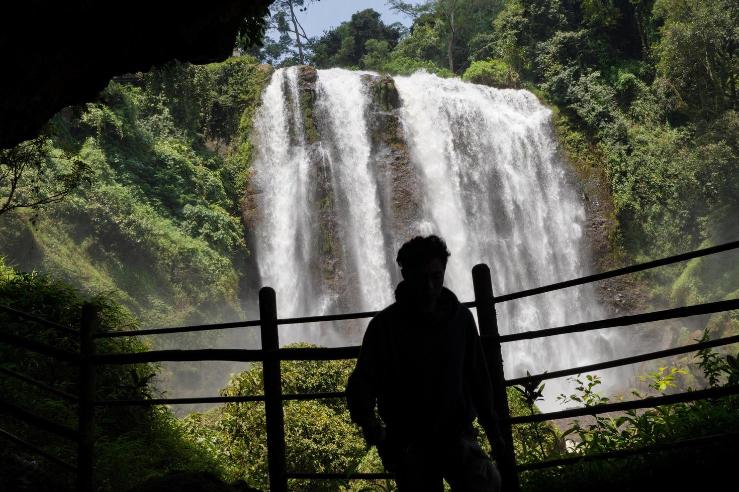 Silhouette man on the cave in front of great water fall, Semarang Central Java. The photo is suitable to use for adventure content media, nature poster and forest background.