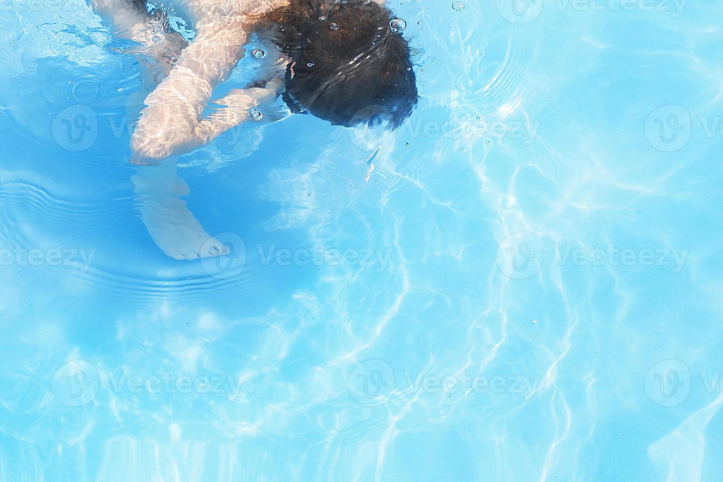 chico inmersiones en nadando piscina . chico nada en el piscina. niño aprendizaje a nadar foto