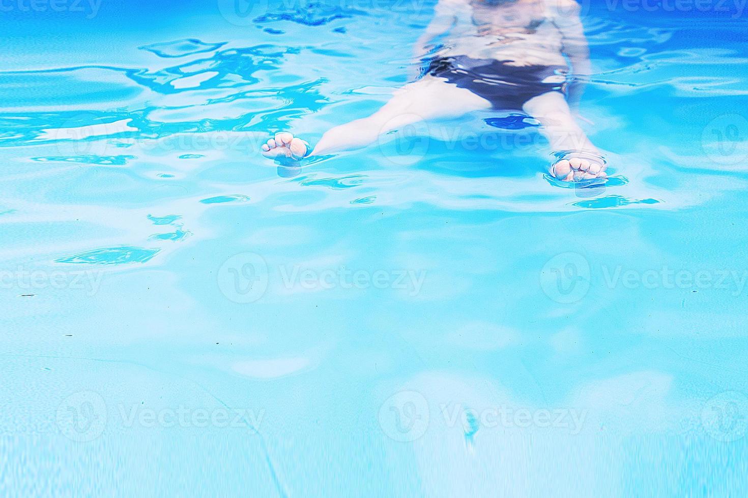 chico nada en el piscina. chico aprendizaje a nadar. pies en el piscina cerca foto