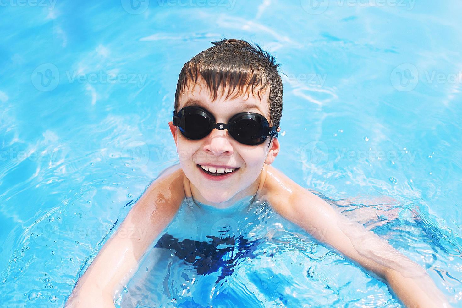 contento bebé en el piscina. chico nada en el piscina con nadando lentes. . chico aprendizaje a nadar foto