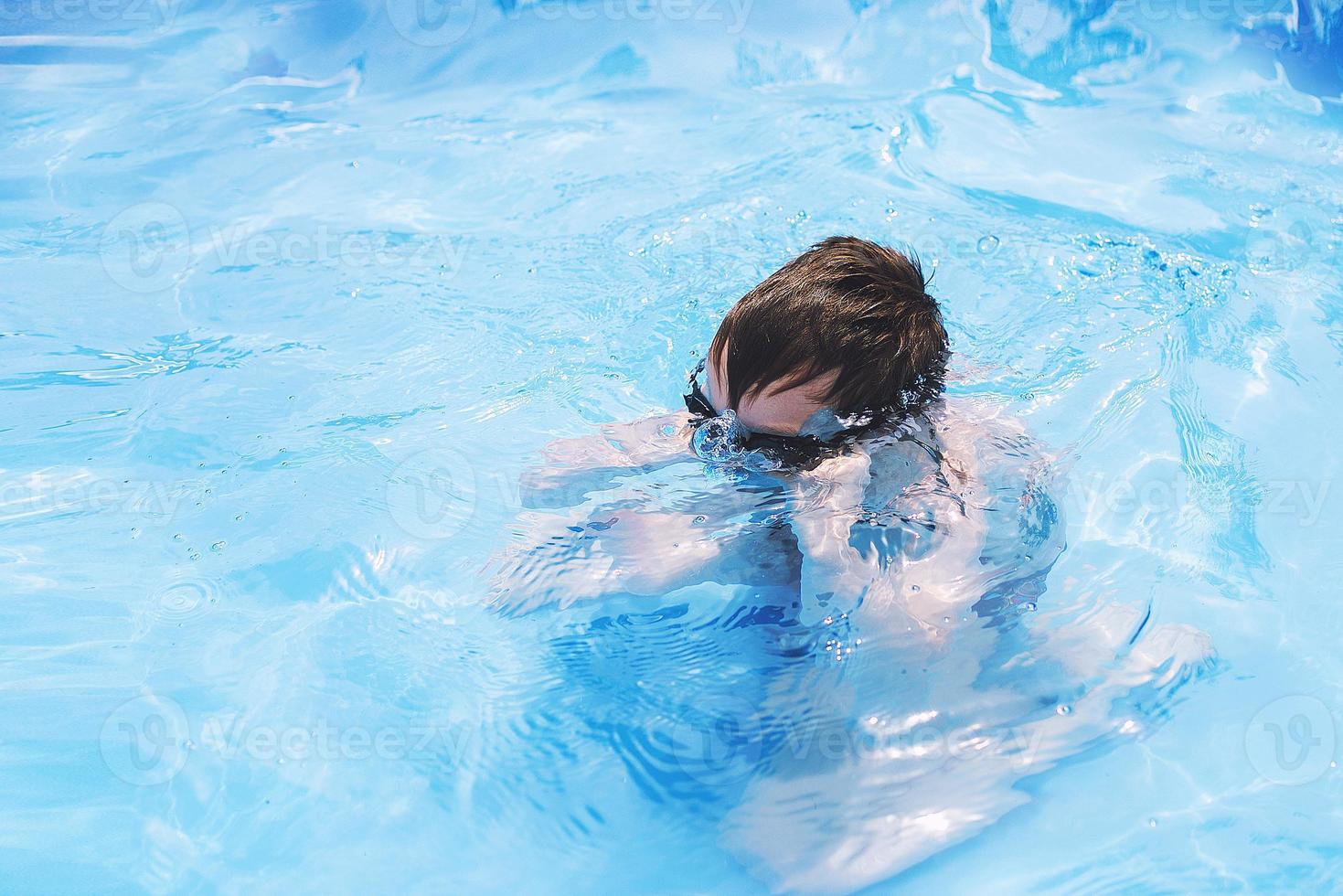 boy dives in swimming pool with swimming glasses. boy swims in the pool. child learning to swim photo