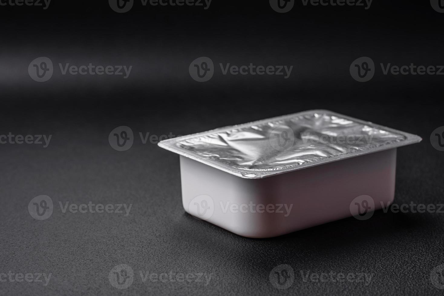 Rectangular plastic box with yogurt or cheese hermetically sealed with a foil lid photo