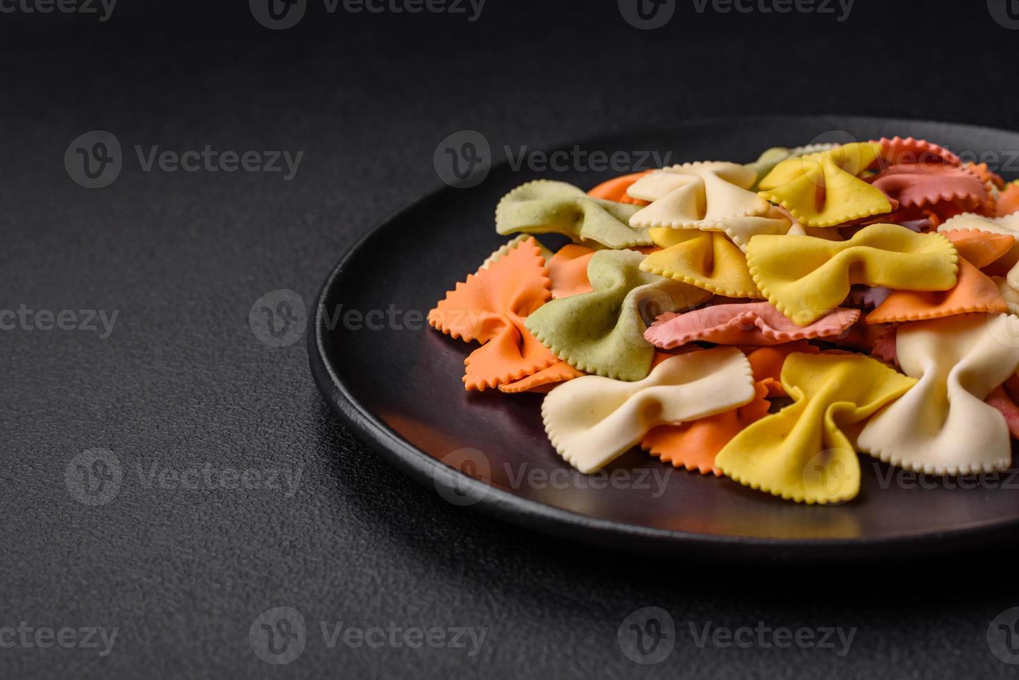 Raw farfalle pasta in different colors on a dark concrete background photo