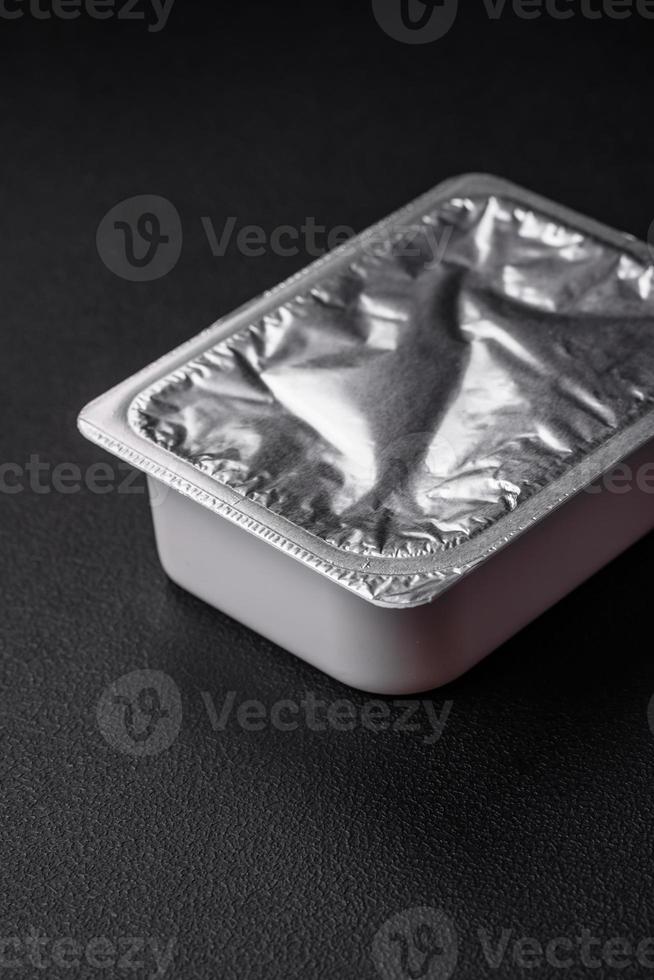 Rectangular plastic box with yogurt or cheese hermetically sealed with a foil lid photo