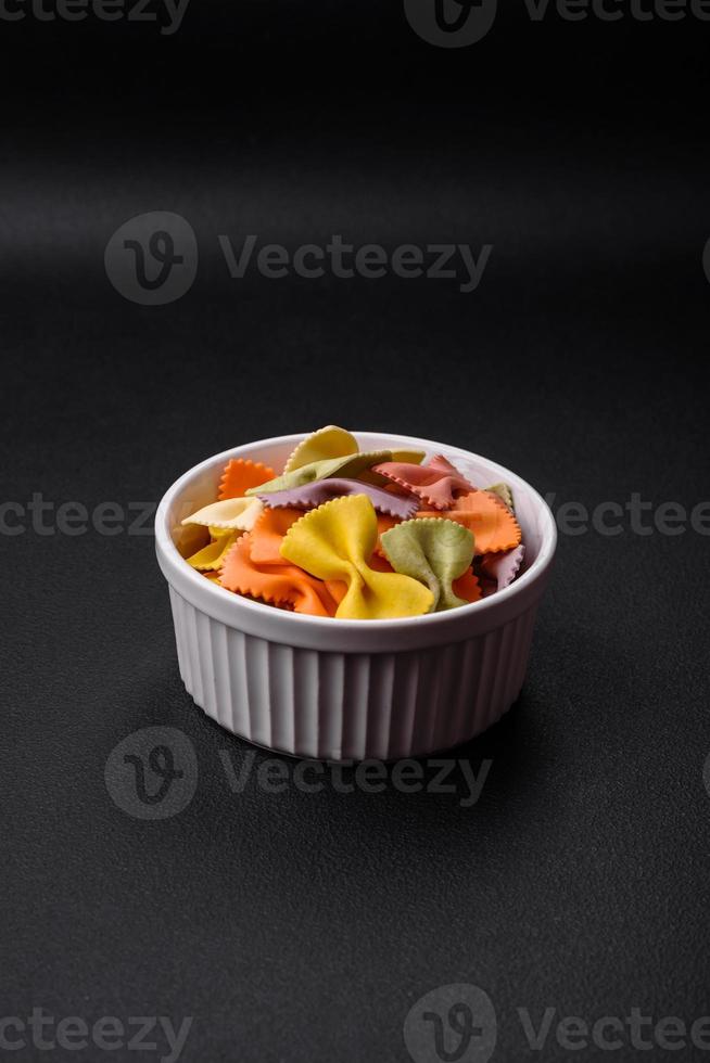 Raw farfalle pasta in different colors on a dark concrete background photo