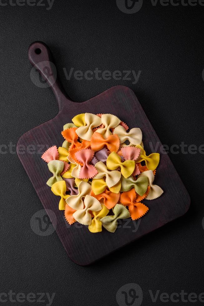 crudo farfalle pasta en diferente colores en un oscuro hormigón antecedentes foto