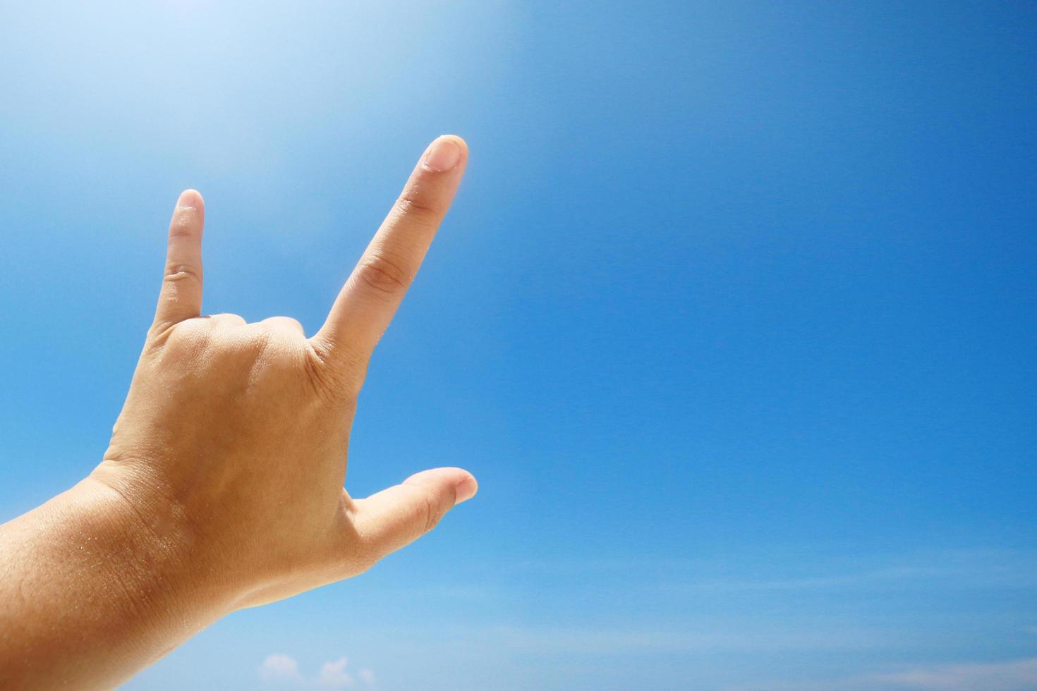 Hand sign of love and showing fingers means I love you on blue sky with sunlight and copty space. photo